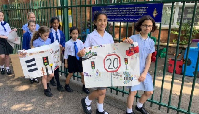 Children walking in pairs along a pavement carrying banners asking for 20mph speed limits and safe places to cross roads.
