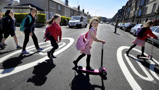 Group of children crossing the road, walking and riding scooters