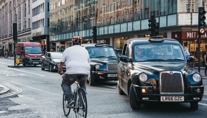 Rear view of person cycling on London street with black cab taxis waiting to turn