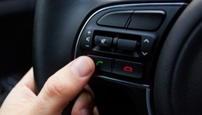 A close-up of buttons on a steering wheel. A person is pressing the 'accept call' button.