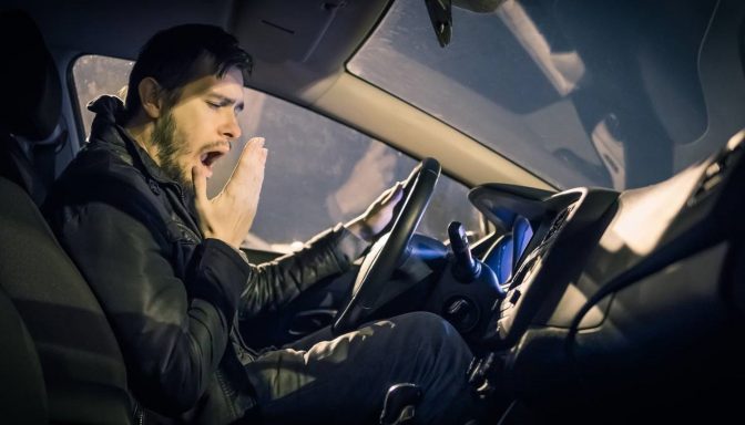 A yawning man sat at the wheel of a car.