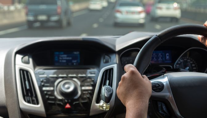 A close up of hands on a steering wheel, as they drive along the motorway.