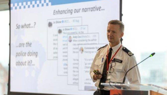 A police commander in uniform speaking at a lectern at a conference.