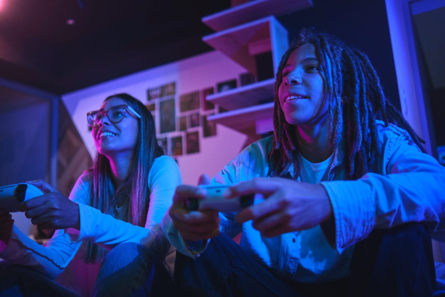 Two smiling young people sit next to each other on a sofa, playing a video game.