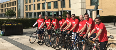 A cheerful group of men on bicyles and dressed in red t-shirts pose for a photograph.