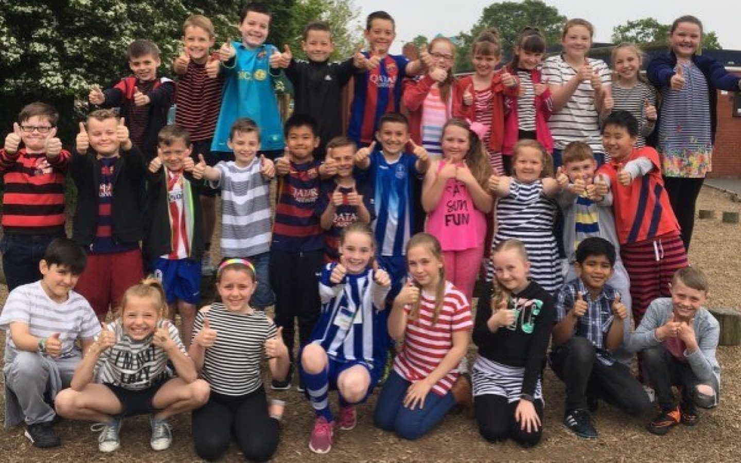 A group of young schoolchildren posing for a photo. They look happy and are wearing stripy t-shirts.