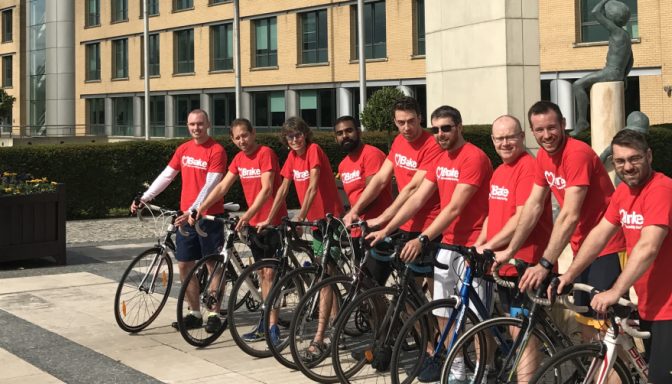 A cheerful group of men on bicyles and dressed in red t-shirts pose for a photograph.