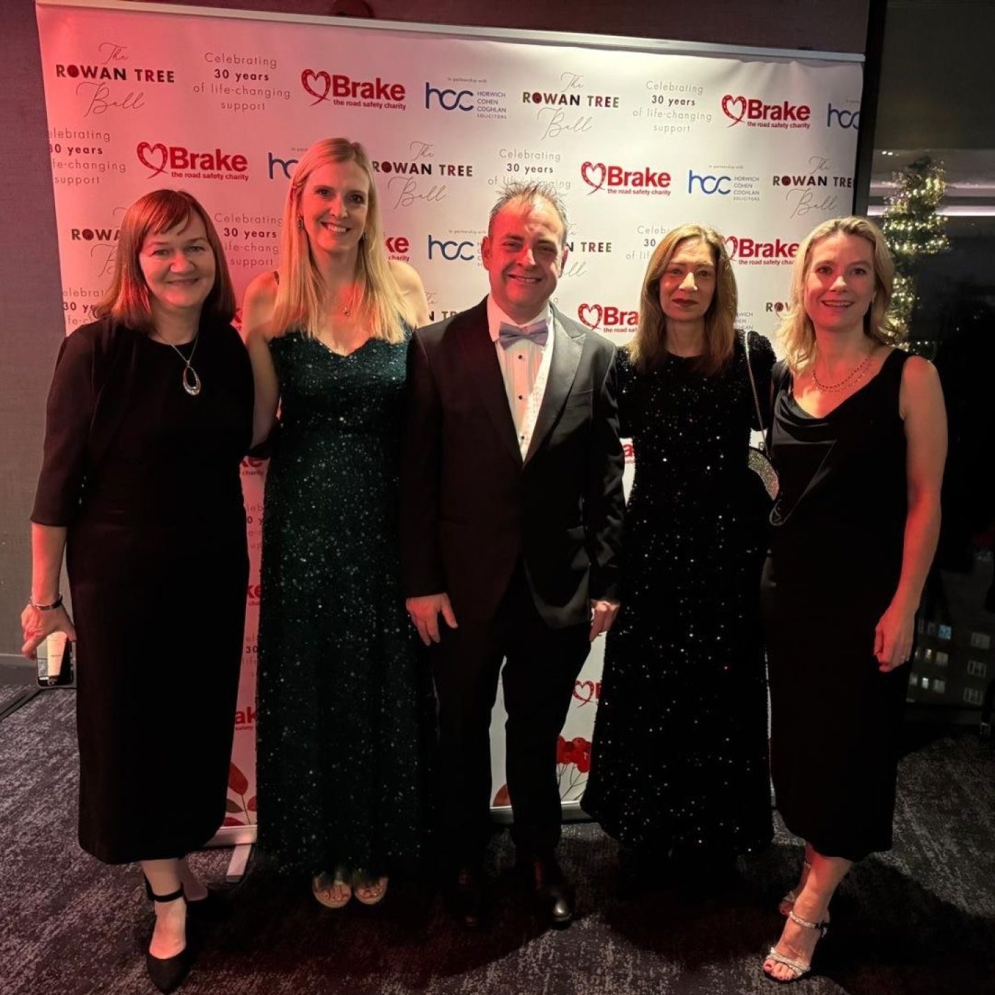 Four women and a man in formal dress pose for a photograph at an event.
