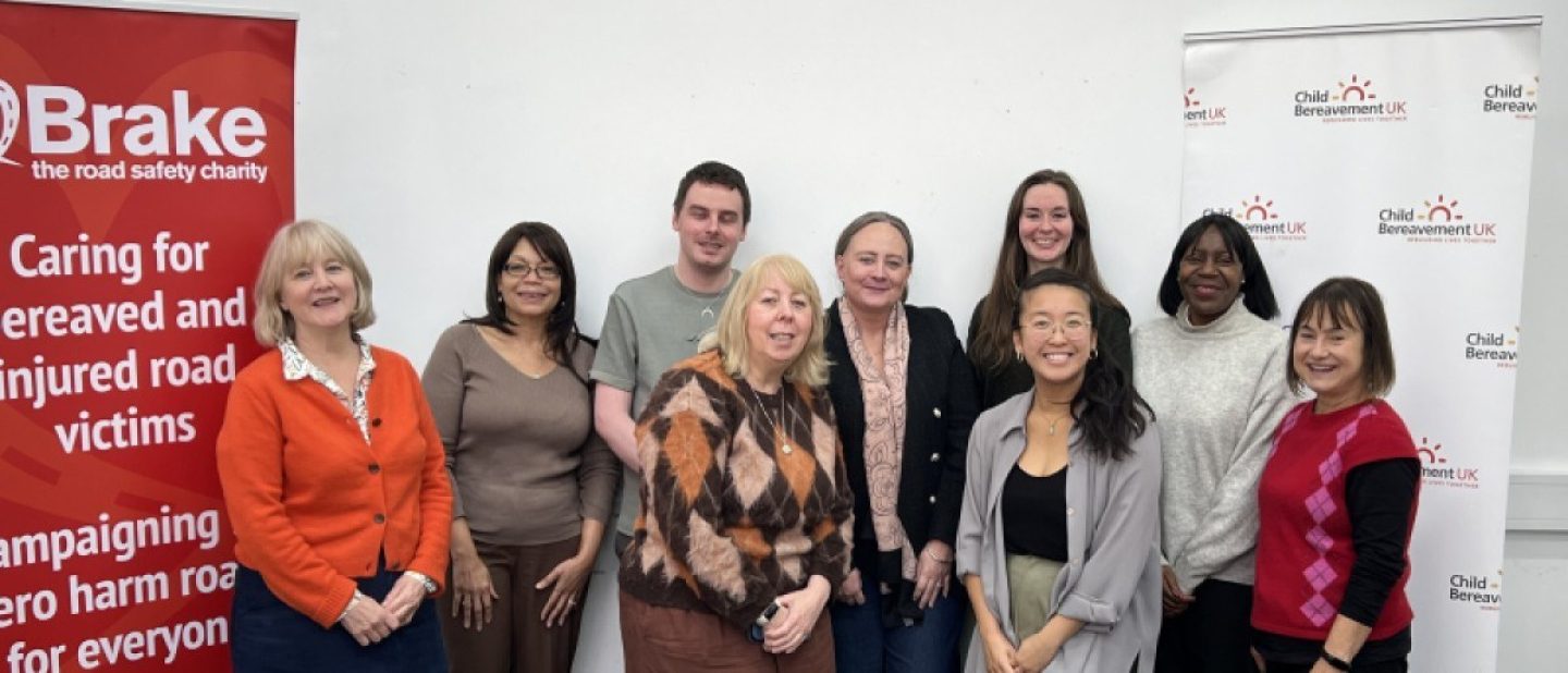 A group of people pose for a photo between banners advertising Brake, the road safety charity and Child Bereavement UK.