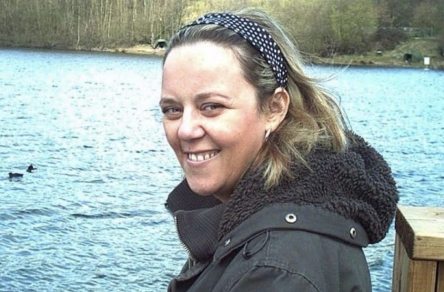 A woman smiles and poses for a photograph in front of a lake.