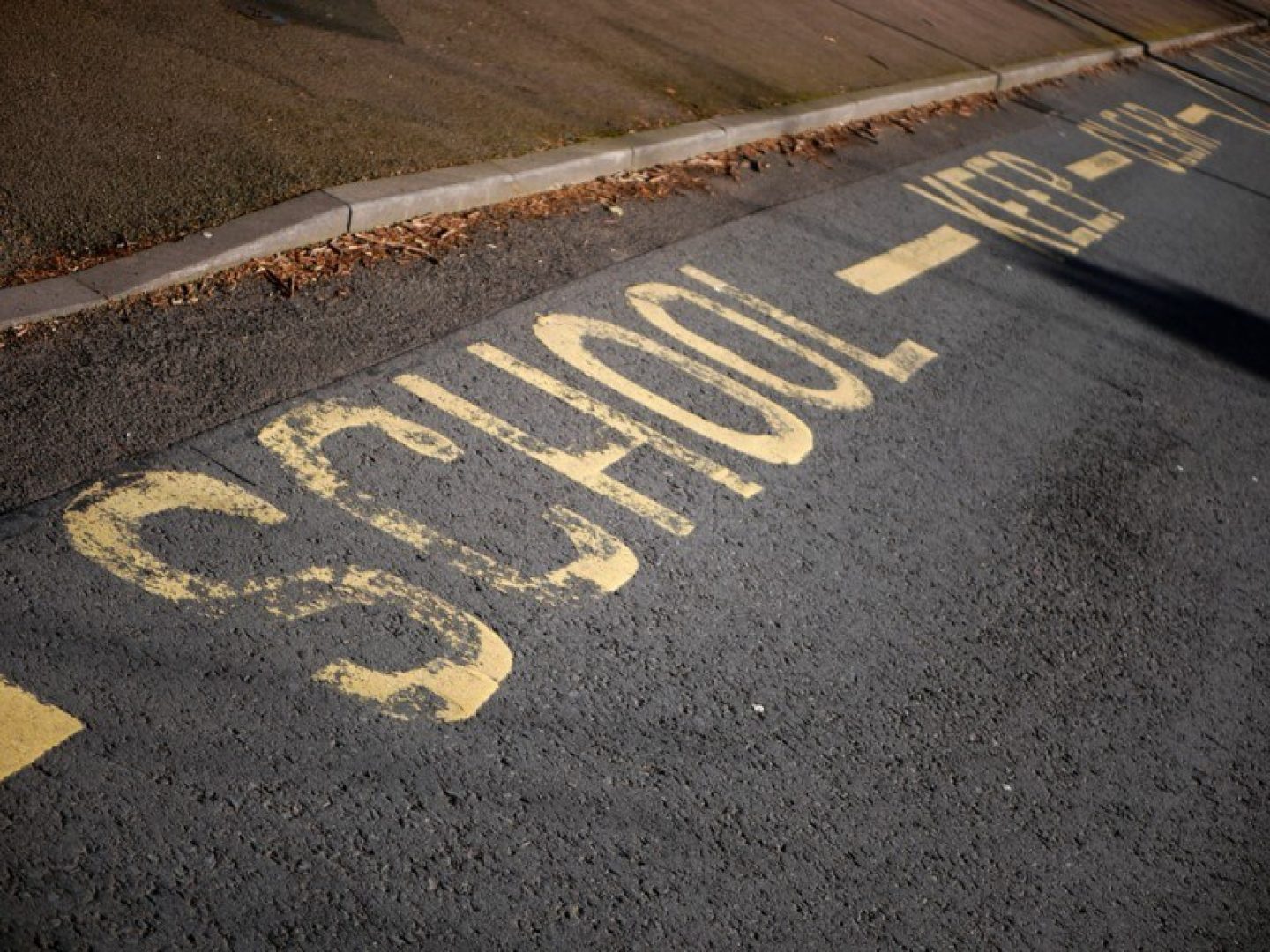 A road next to a pavement, painted with yellow writing which says "School. Keep clear."