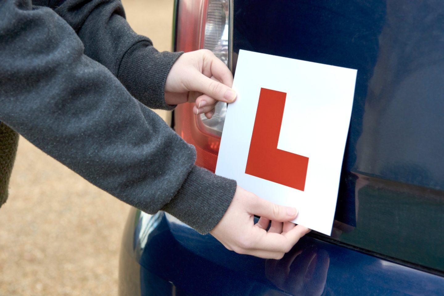 A young person attaching an L plate to the back of a car, alerting other road users that they are a learner driver.