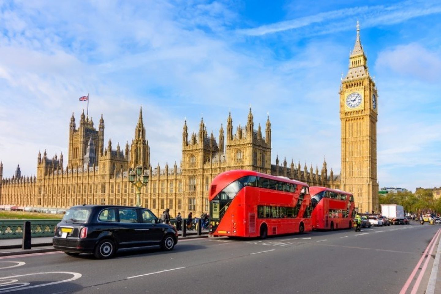 Big Ben and the Palace of Westminster on a sunny day in London, with a red double-decker bus and a black car on the street.