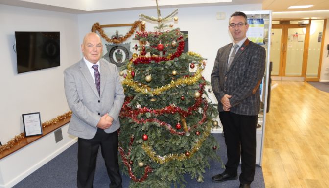 Two smartly dressed professional men, standing either side of a Christmas tree