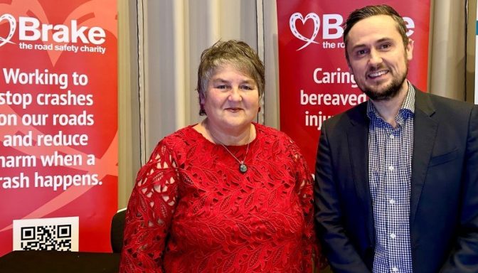 A smiling older woman next to a smiling middle-aged man, posing for a photo next to banners with Brake, the road safety charity's logo on.