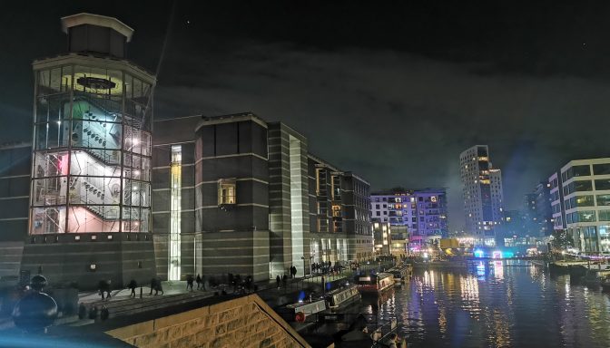A night-time long exposure photograph of the Royal Armouries Museum in Leeds, illuminated and reflected in the calm waters of Leeds Dock