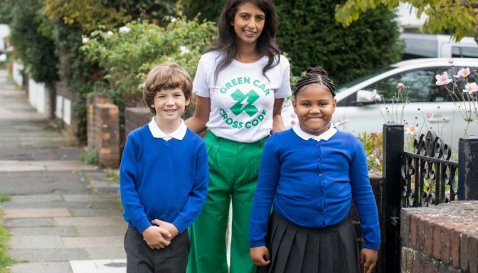 A woman posing for a photograph with two children in school uniform. The woman is wearing a t-shirt which says: Green car cross code