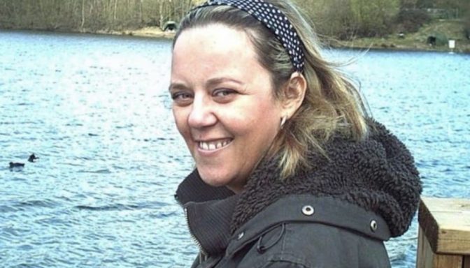 A woman smiles and poses for a photograph in front of a lake.