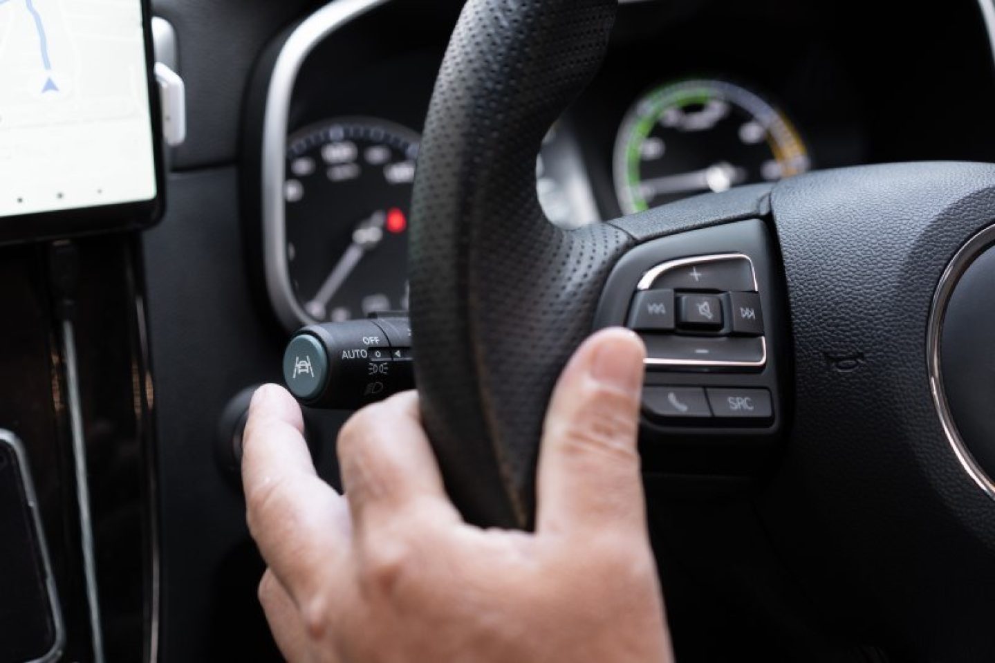 A close up image of a car's steering wheel. The person driving is reaching to press the lane keeping assist button, to turn the function on or off.