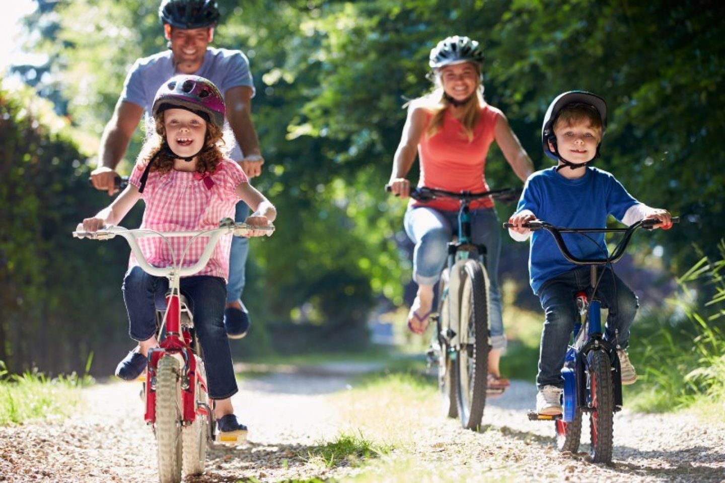 A man, woman, and two children are cycling. They are on a wide forest track, with no traffic, and are wearing helmets.