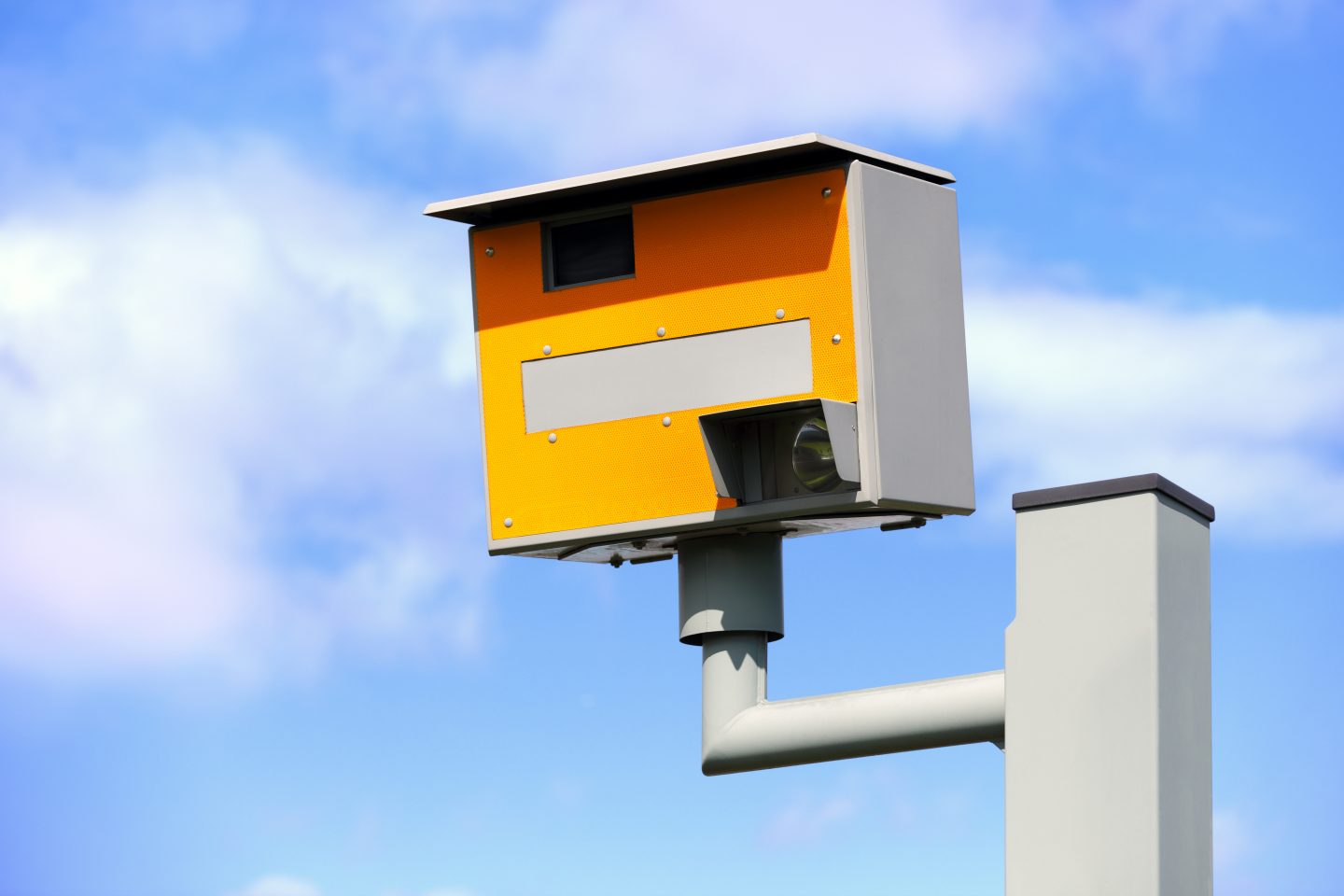 A yellow speed camera, with a blue sky in the background.