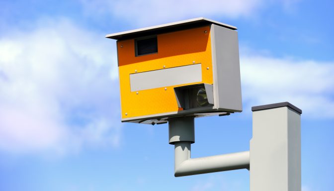 A yellow speed camera, with a blue sky in the background.