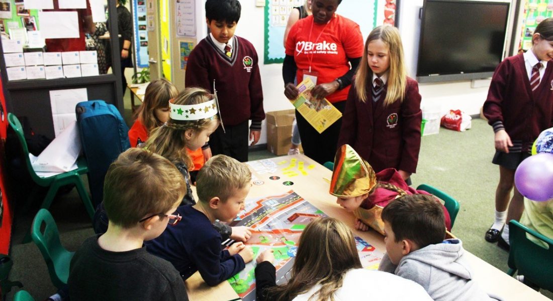 A group of schoolchildren in a classroom. They are with a woman wearing a Brake, the road safety charity t-shirt and they appear to be taking part in road safety activities.