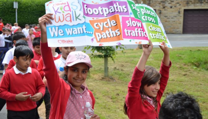 Children holding colorful signs in front of a school building, smiling and showing support for a cause.