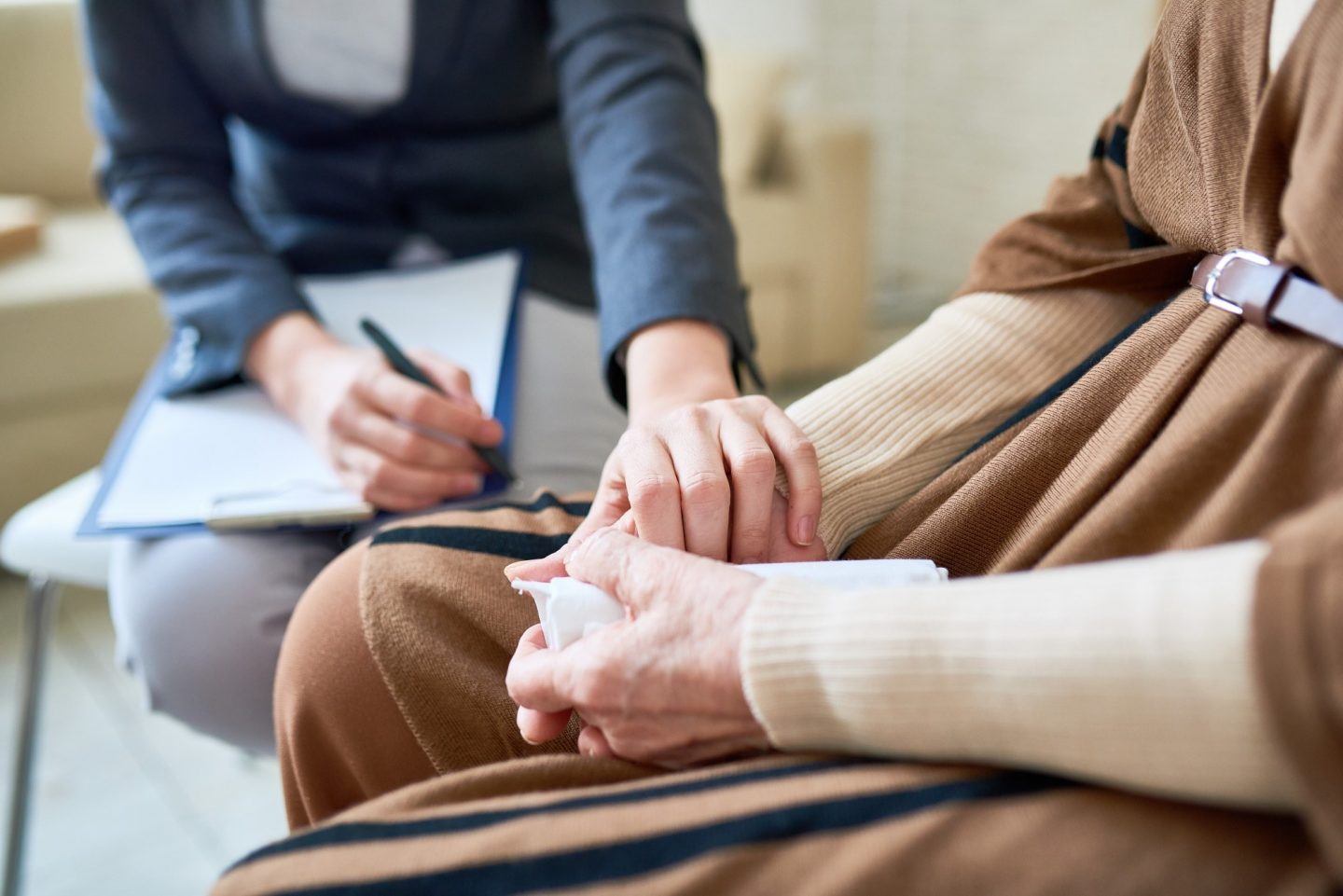 A woman gently holds the hand of an older woman, conveying a sense of care and connection between them.