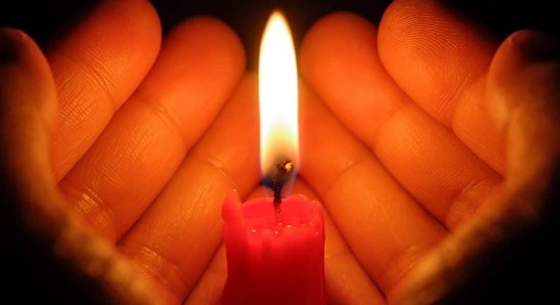 A close-up of two hands cupped around a lit candle.