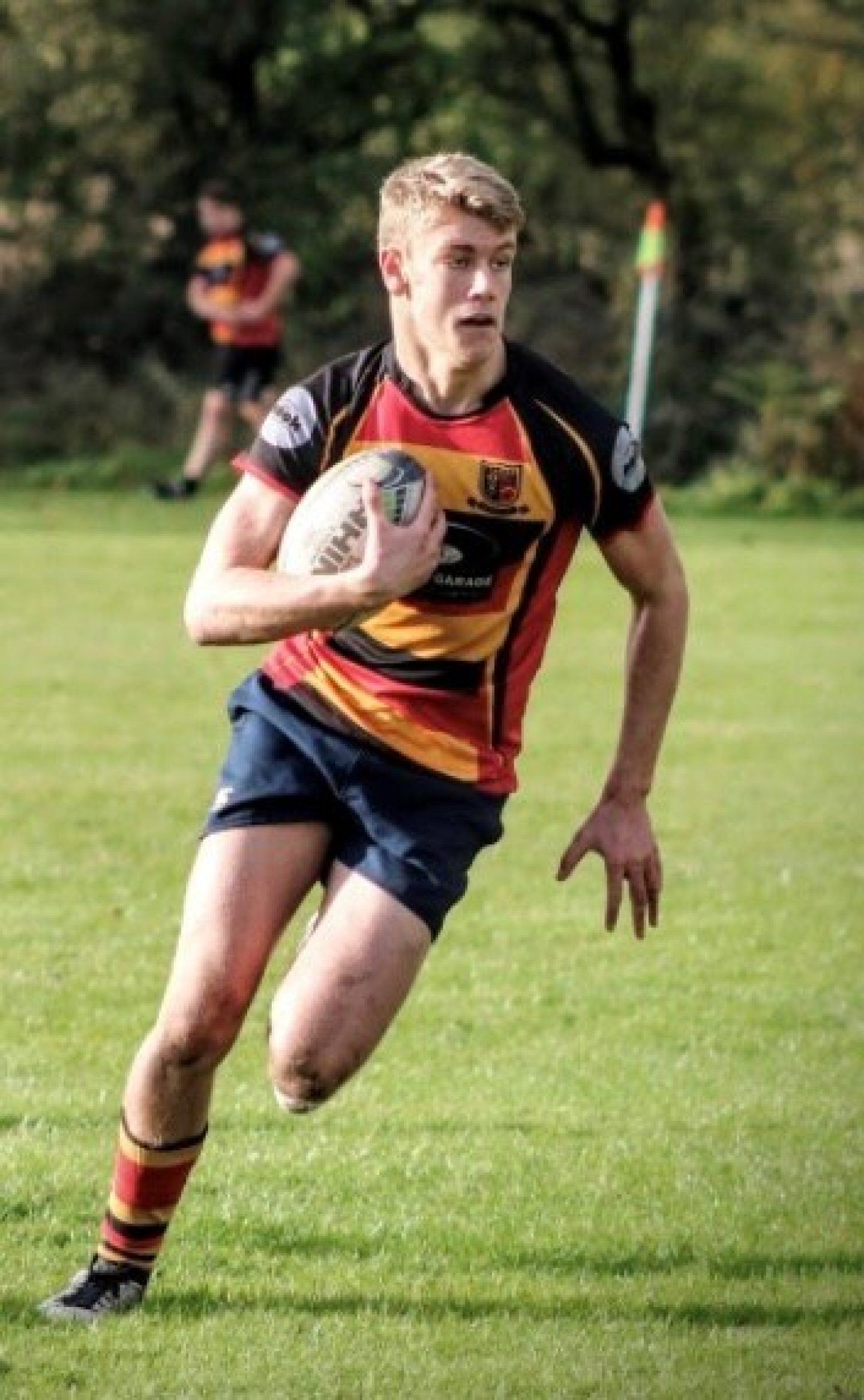 A young man on a rugby field, running with the ball.