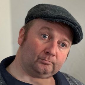 A close-up image of a man wearing a flat cap.