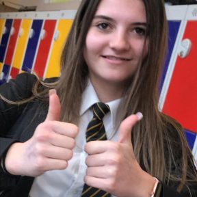 A young girl poses for a photograph in front of lockers at school.