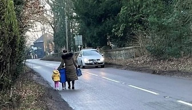 A mother and two young children, walking along a road with no pavement. There is a car coming the other way.